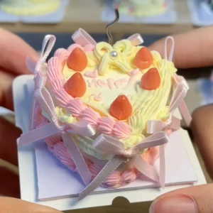 Finished example of a DIY miniature clay heart cake kit with pastel pink piping, pale yellow cream-style details, strawberry-like toppings, and ribbon accents