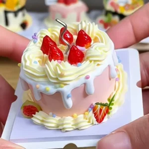 Sample finished piece from a DIY Miniature Strawberry Drip Cake Kit featuring pink cake layers, cream-style piping, white drip decoration, and strawberry accents.